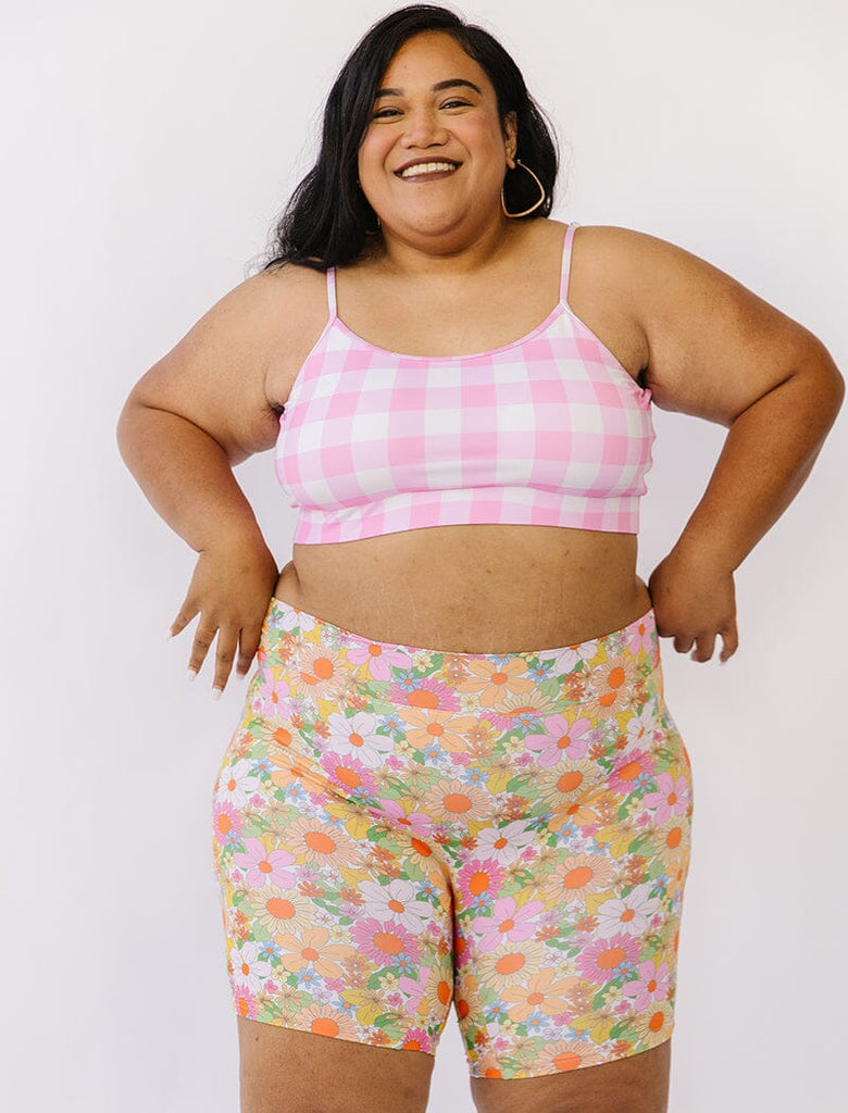 Photo of woman wearing pink gingham bralette swim top with multi colored long swim shorts