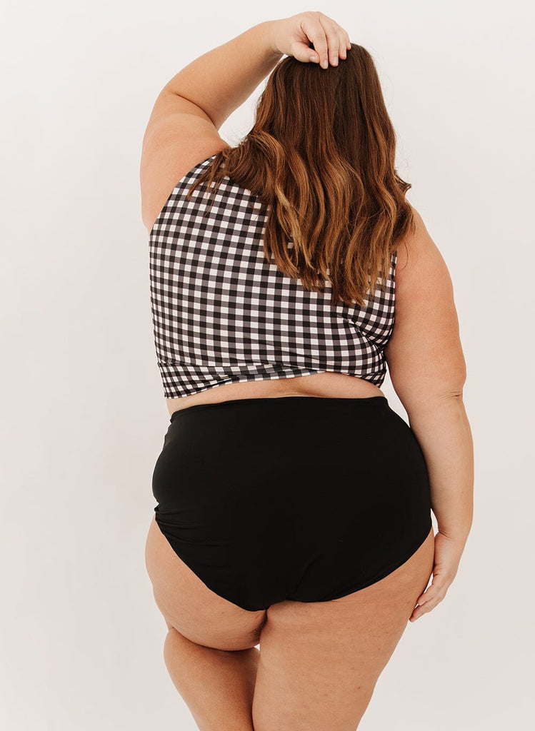 Photo of a woman wearing black ultra high-waist swim bottoms with a black gingham knotted crop swim top back angle