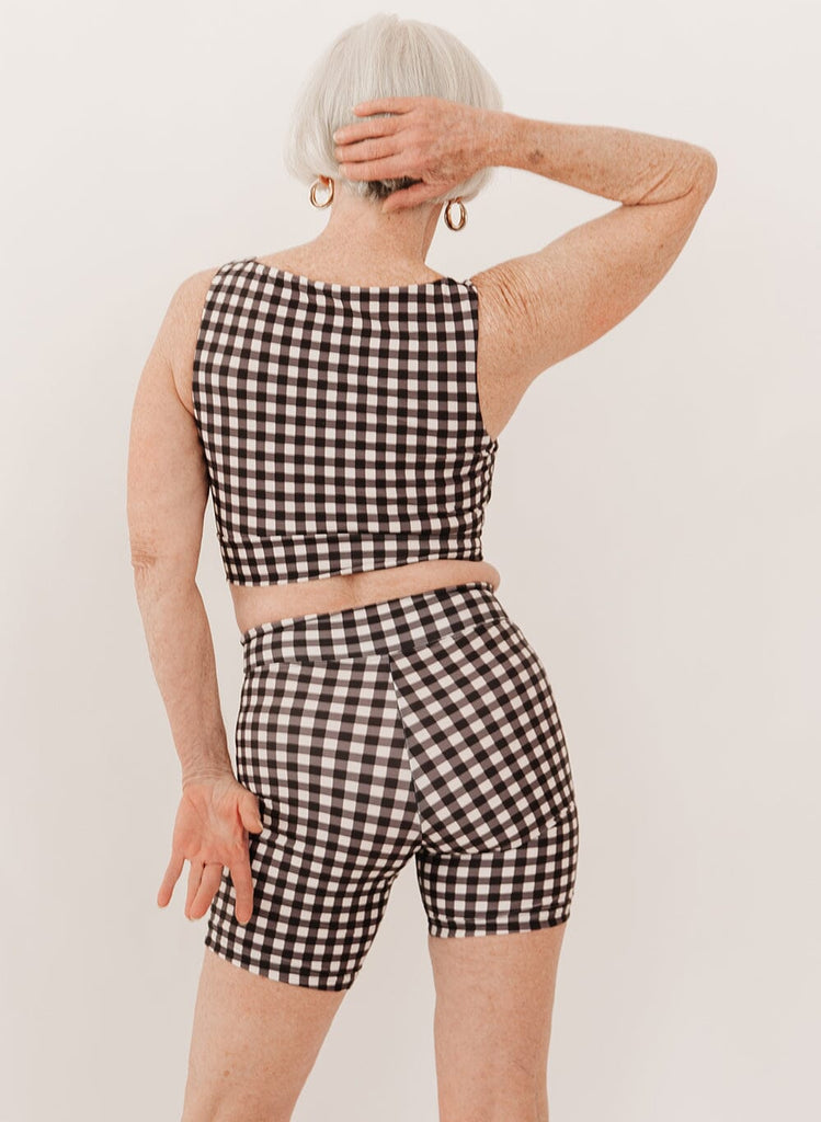 Photo of a woman wearing a black gingham knotted swim crop top with black gingham swim short bottoms back angle