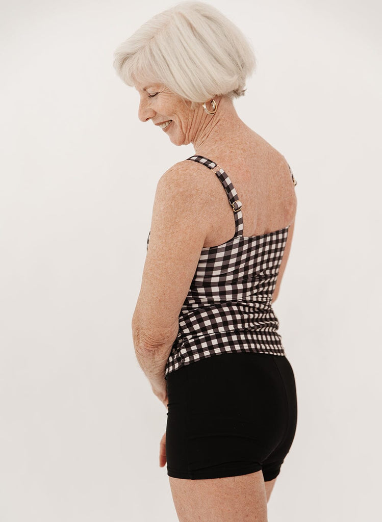 Photo of a woman wearing high-waist black swim shorts and a black gingham square neck tankini swim top side angle