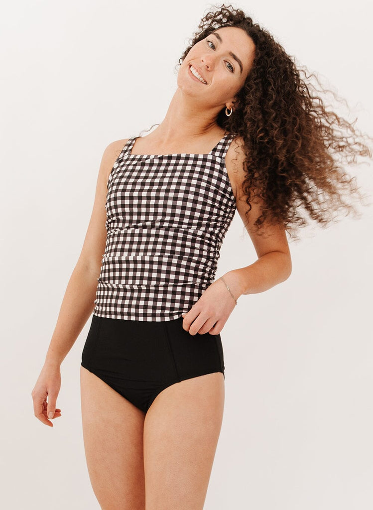 Photo of a woman wearing black high-waist swim bottoms with a black gingham square neck tankini swim top