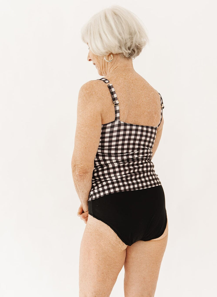 Photo of a woman wearing black ultra high-waist swim bottoms with a black gingham square neck tankini swim top back angle