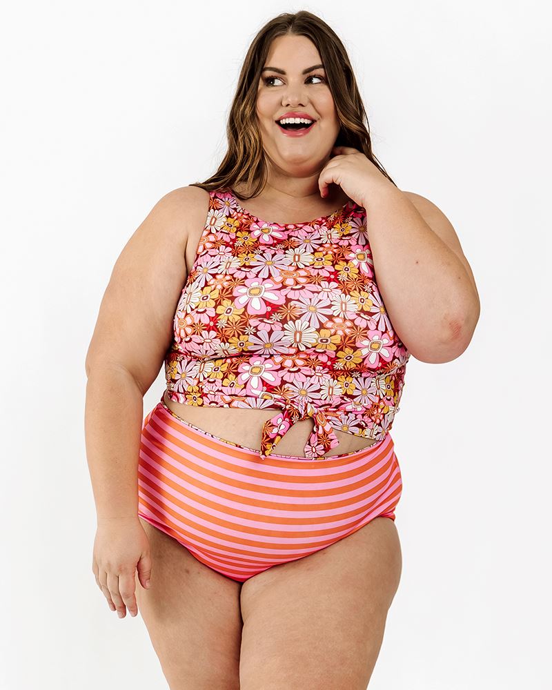 Photo of a woman wearing a Groovy Blooms floral knotted swim crop top and an orange and pink stripe swim bottom