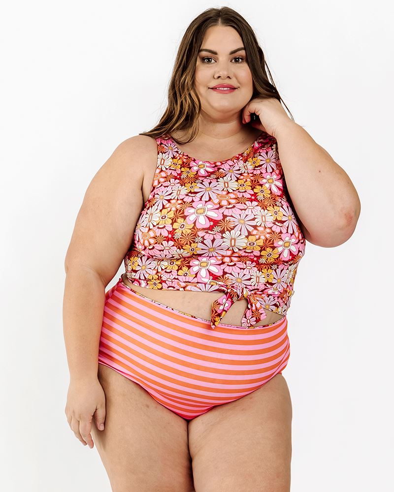 Photo of a woman wearing a Groovy Blooms/sherbet stripe reversible swim bottom stripe side and a groovy Blooms floral swim crop top