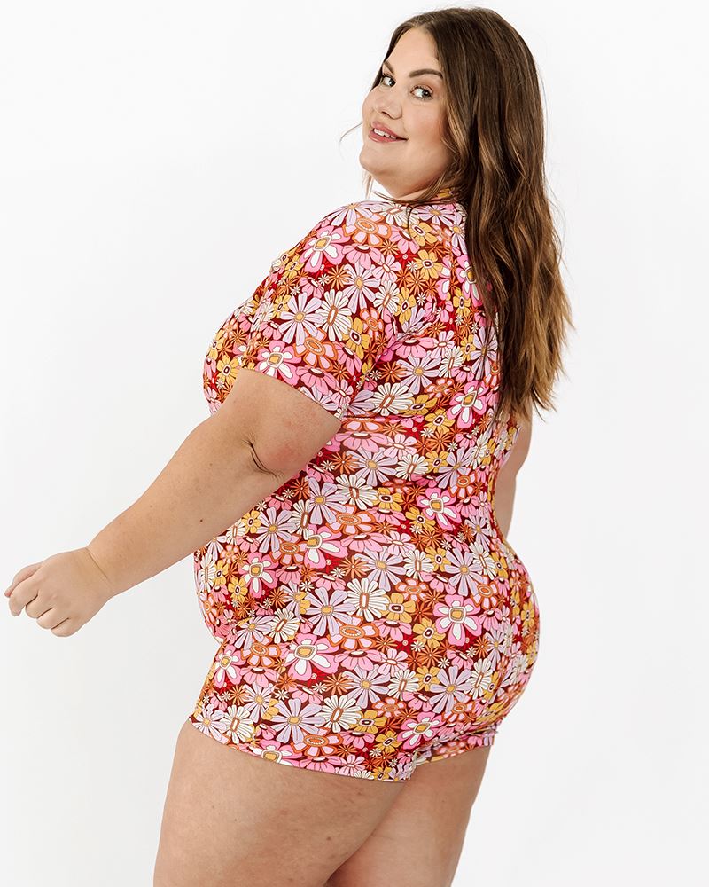 Photo of a woman wearing a groovy Blooms floral rash guard one-piece swim suit side angle