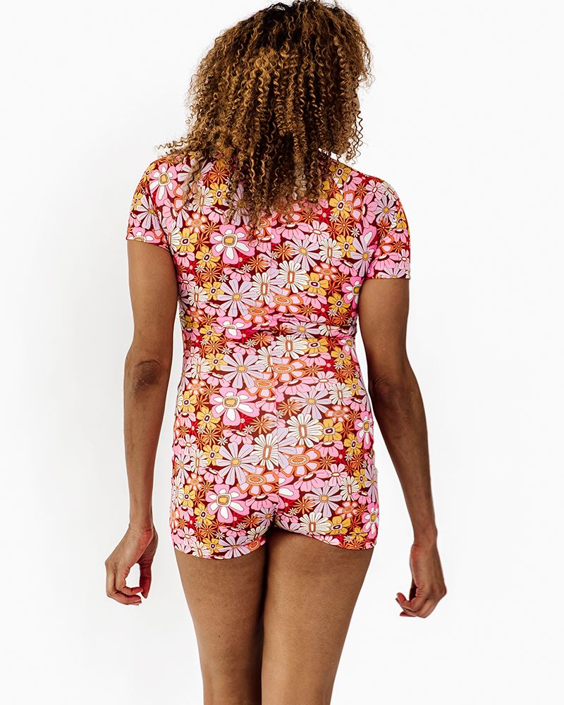 Photo of a woman wearing a groovy Blooms floral rash guard one-piece swim suit back angle