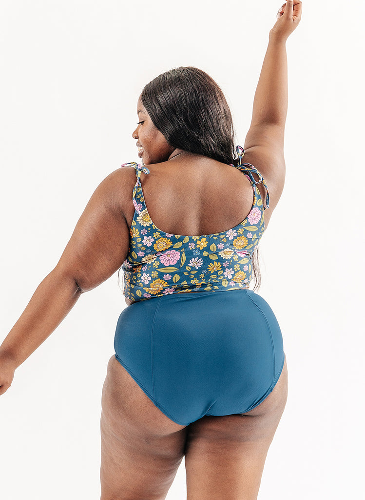 Photo of woman wearing multi color floral cropped swim top with blue swim bottoms back angle