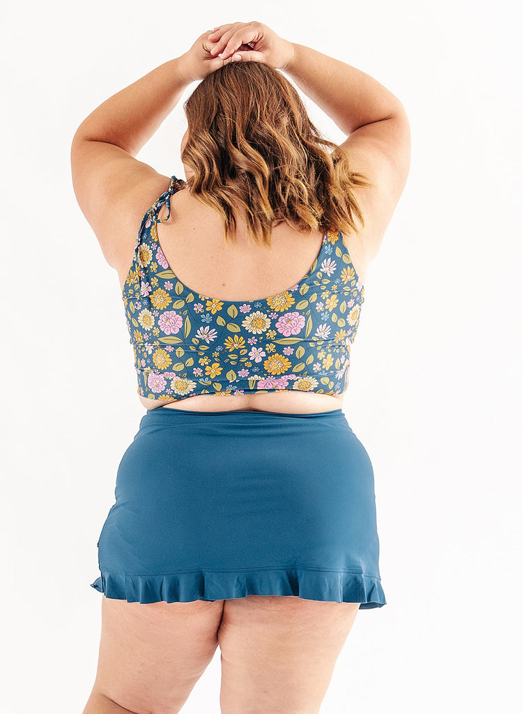 Photo of woman wearing multi color floral cropped swim top with blue swim skirt back angle