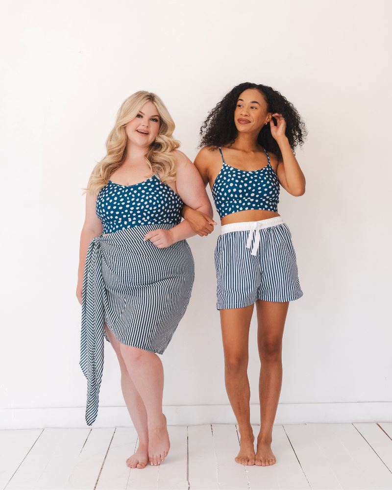 Photo of two women wearing blue and white stripe swim board shorts and a blue and white dotted swim bralette and a blue and white stripe sarong