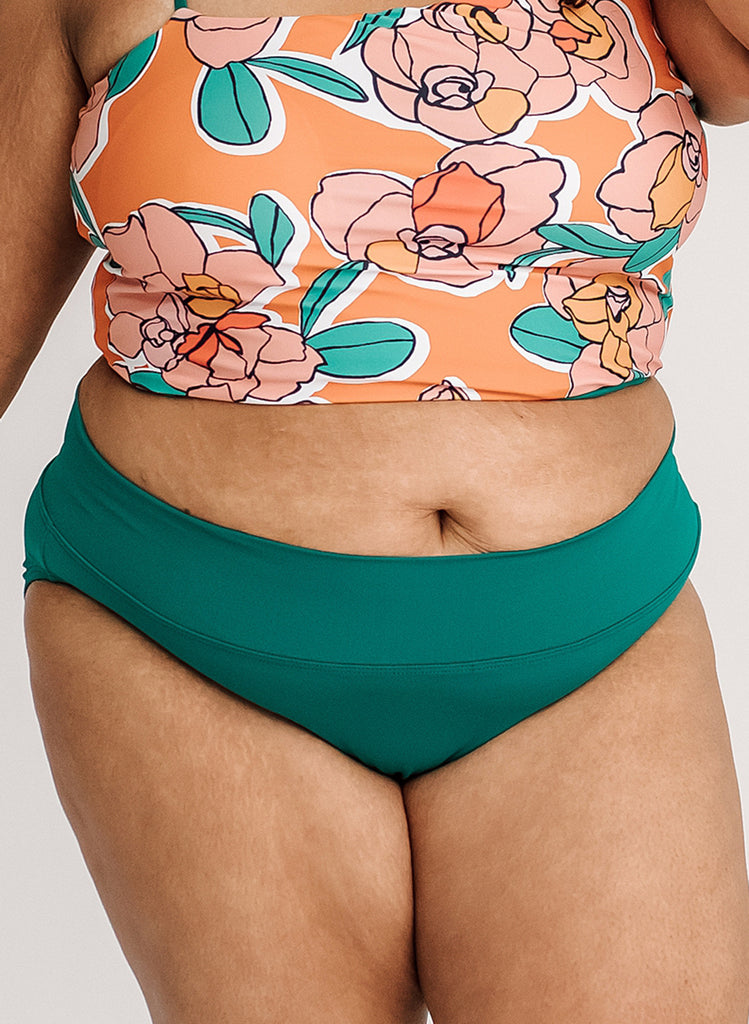 Close up photo of woman wearing an orange floral cropped swim top with blue classic low rise swim bottoms