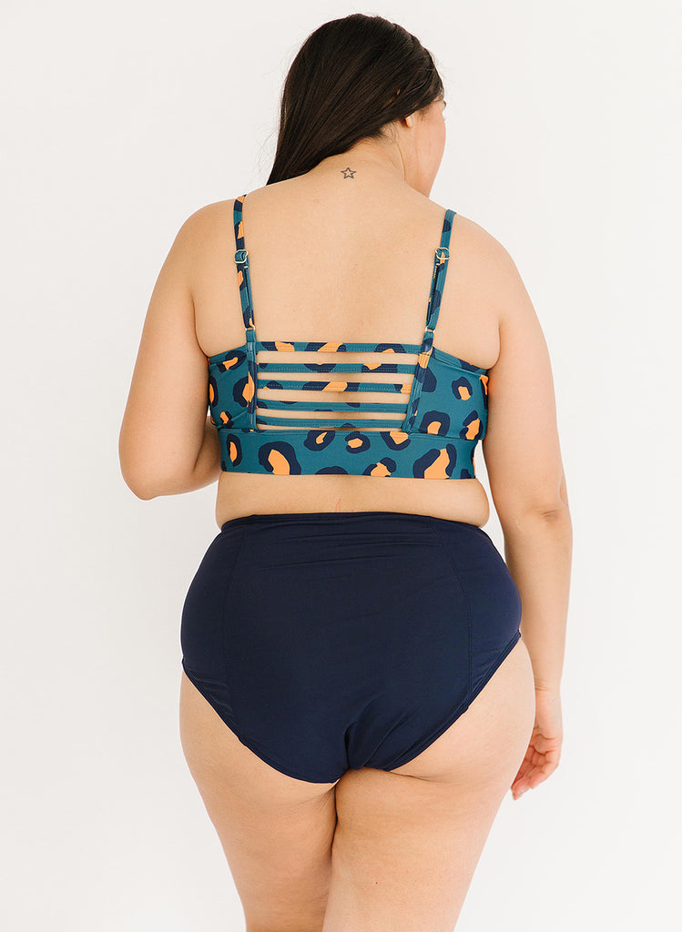 Photo of woman with her back facing us wearing a blue leopard print cropped swim top with blue high waist swim bottoms