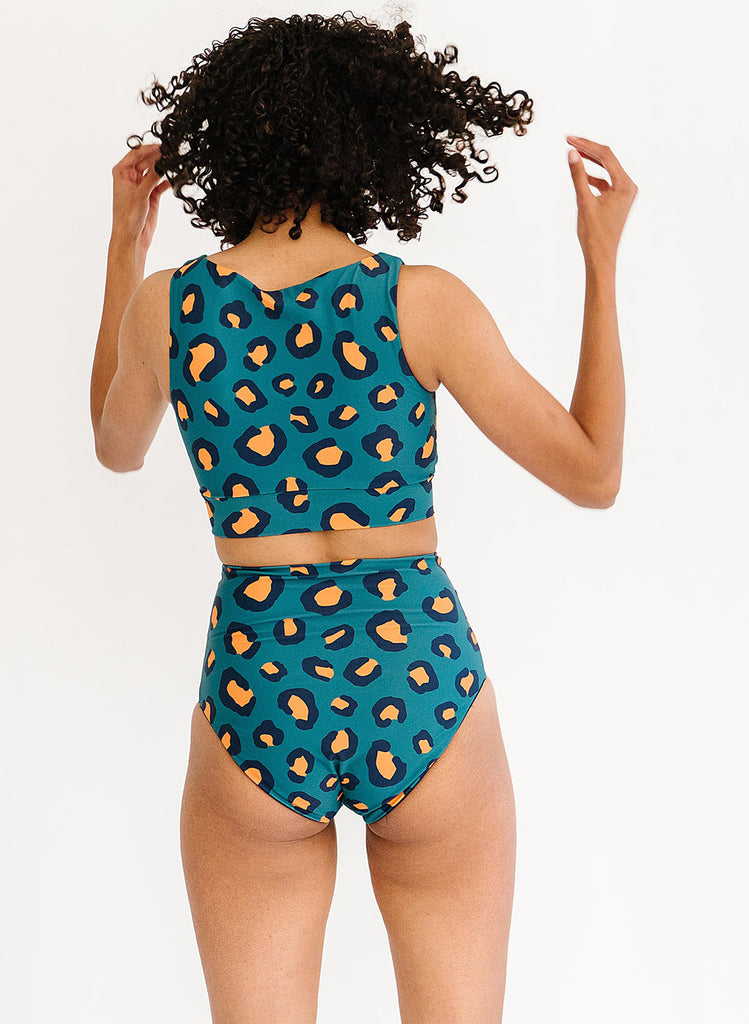 Photo of a woman with her back facing us wearing a blue leopard print cropped swim top with blue leopard print high waist swim bottoms
