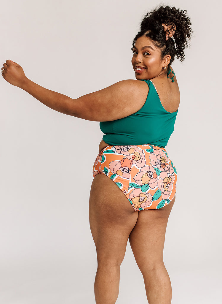 Photo of woman with her back facing us wearing a blue cropped swim top with orange floral high waist swim bottoms