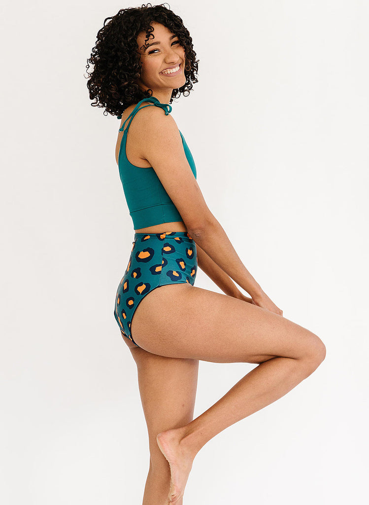 Photo of a woman posing while wearing a blue cropped swim top with blue leopard print high waist swim bottoms