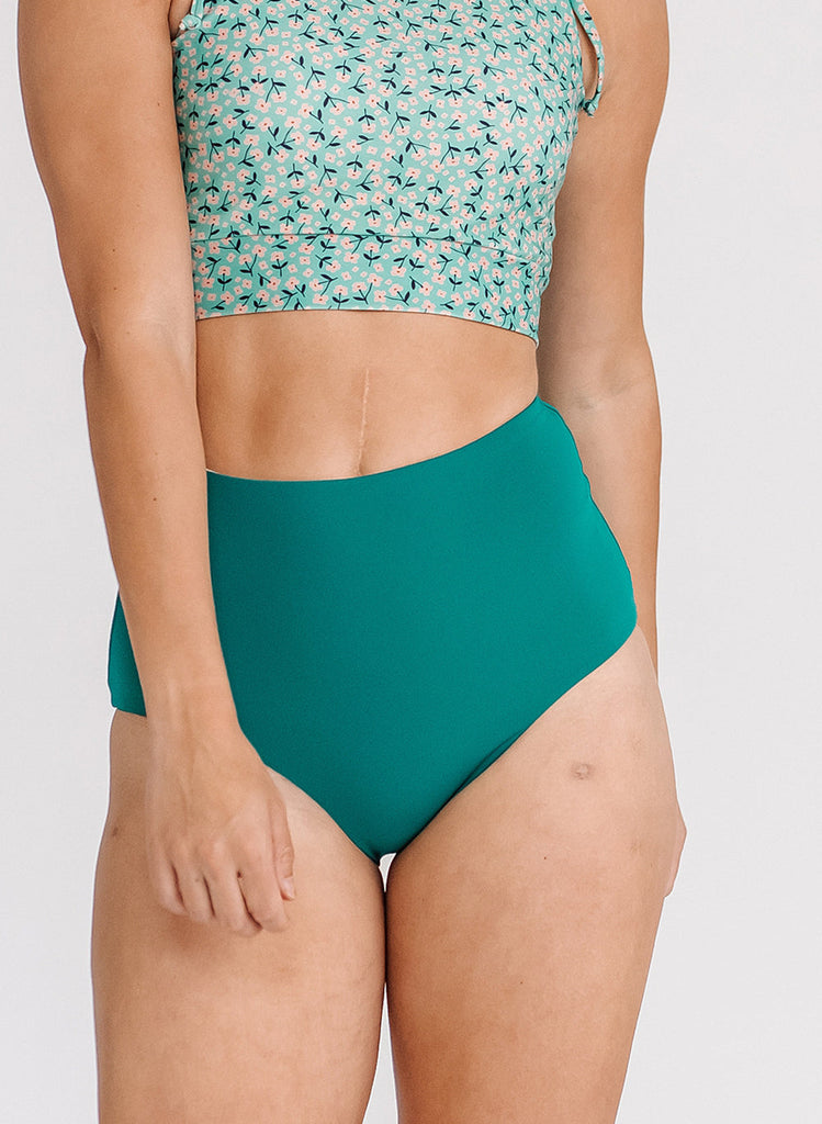 Close up photo of a woman wearing a blue floral cropped swim top with blue high waist swim bottoms