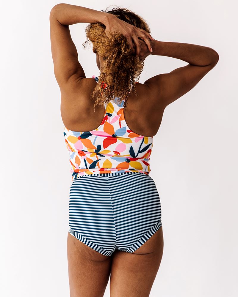 Photo of a woman wearing a June floral swim racer-back swim crop top and an Indigo stripe swim short bottom back angle