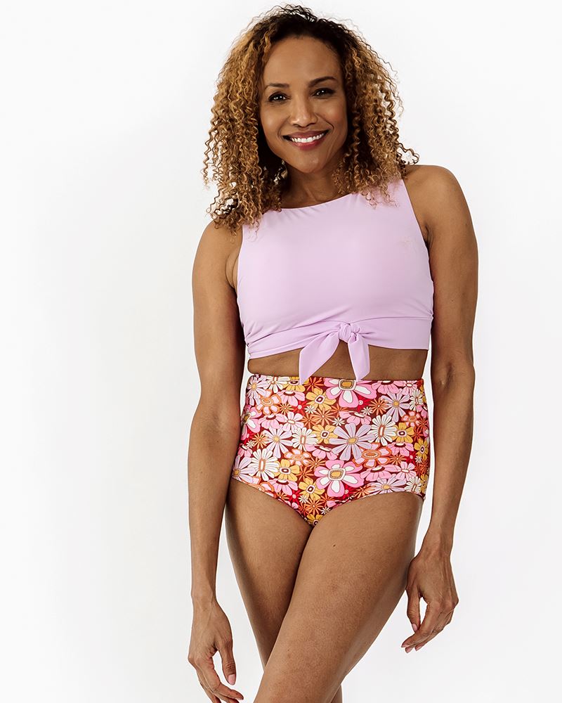 Photo of a woman wearing a Lilac knotted swim crop top and a Groovy Blooms swim bottom