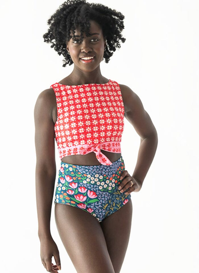 Photo of a woman with her hand on her hip wearing a red floral cropped swim top with blue floral high waist swim bottoms