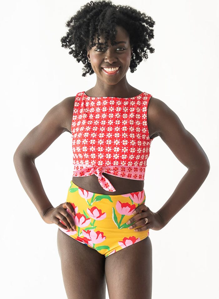 Photo of woman posing with her hands on her hips while wearing a red floral cropped swim top with yellow floral high waist swim bottoms