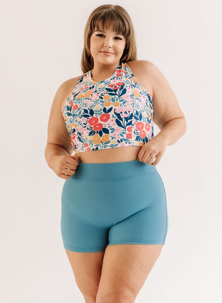 Photo of a woman wearing a May Flowers cross-back swim crop top and an ocean blue swim short bottom