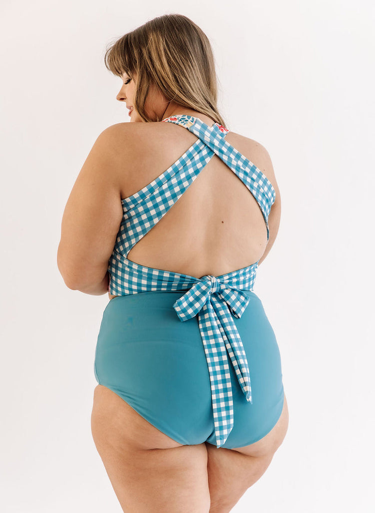 Photo of a woman wearing a May Flowers cross-back swim crop top and an ocean blue swim bottom back angle