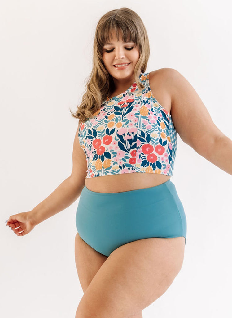 Photo of a woman wearing a May Flowers cross-back swim crop top and an ocean blue swim bottom