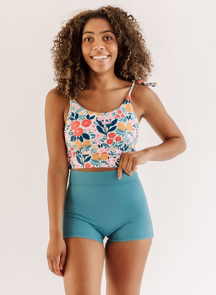 Photo of a woman wearing a may Flowers shoulder-tie swim crop top and an ocean blue swim short bottom