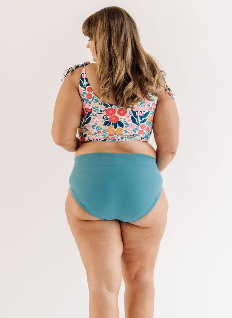 Photo of a woman wearing an Ocean classic swim bottom and a May Flowers swim crop top back angle