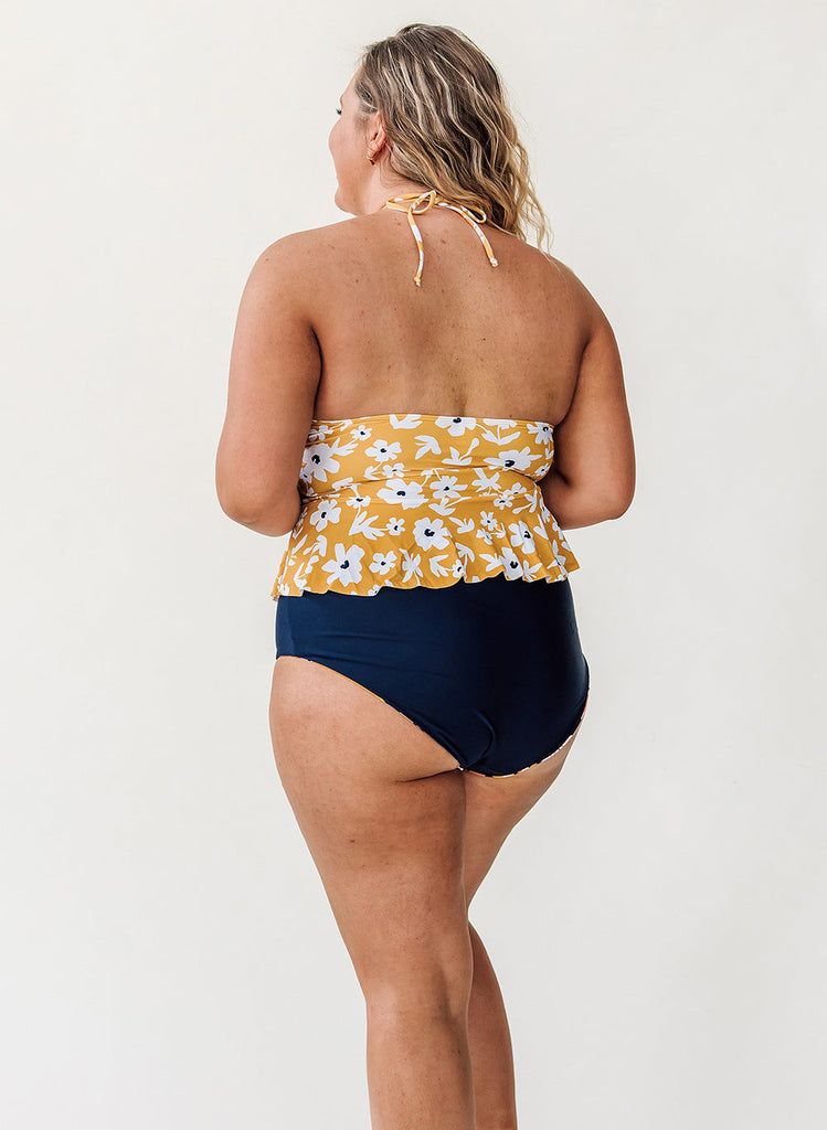 Photo of a woman wearing a yellow floral peplum swim top and a midnight blue swim bottom- back angle