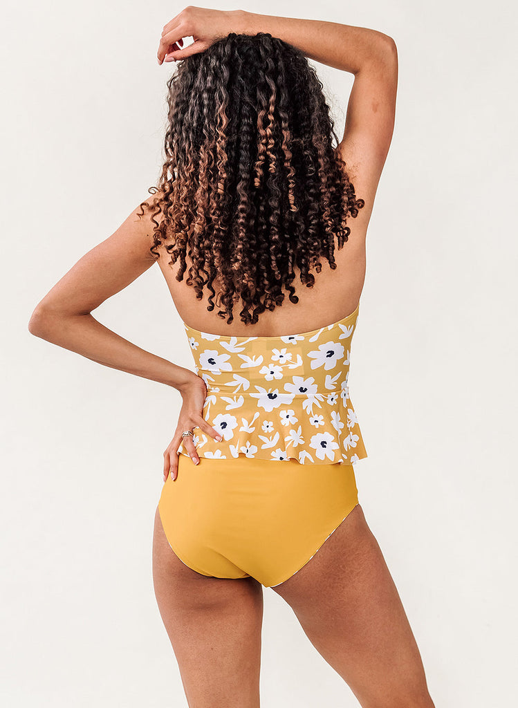 Photo of a woman wearing a yellow floral peplum swim top and a mustard yellow swim bottom- back angle