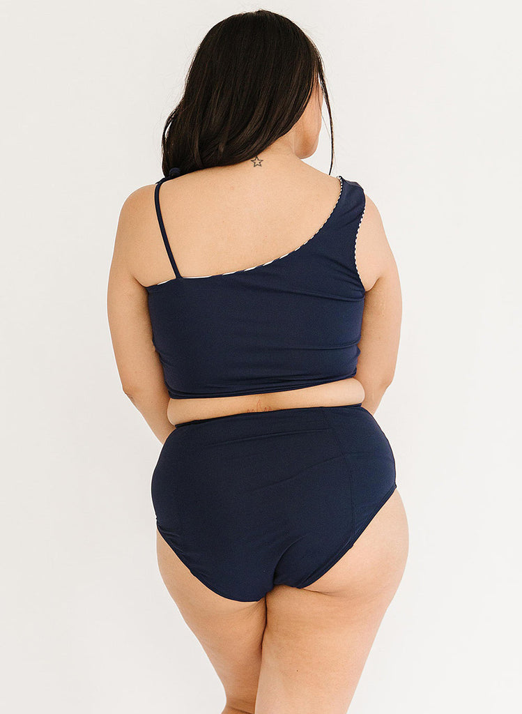 Photo of a woman with her back facing us wearing a blue cropped swim top with blue high waist swim bottoms