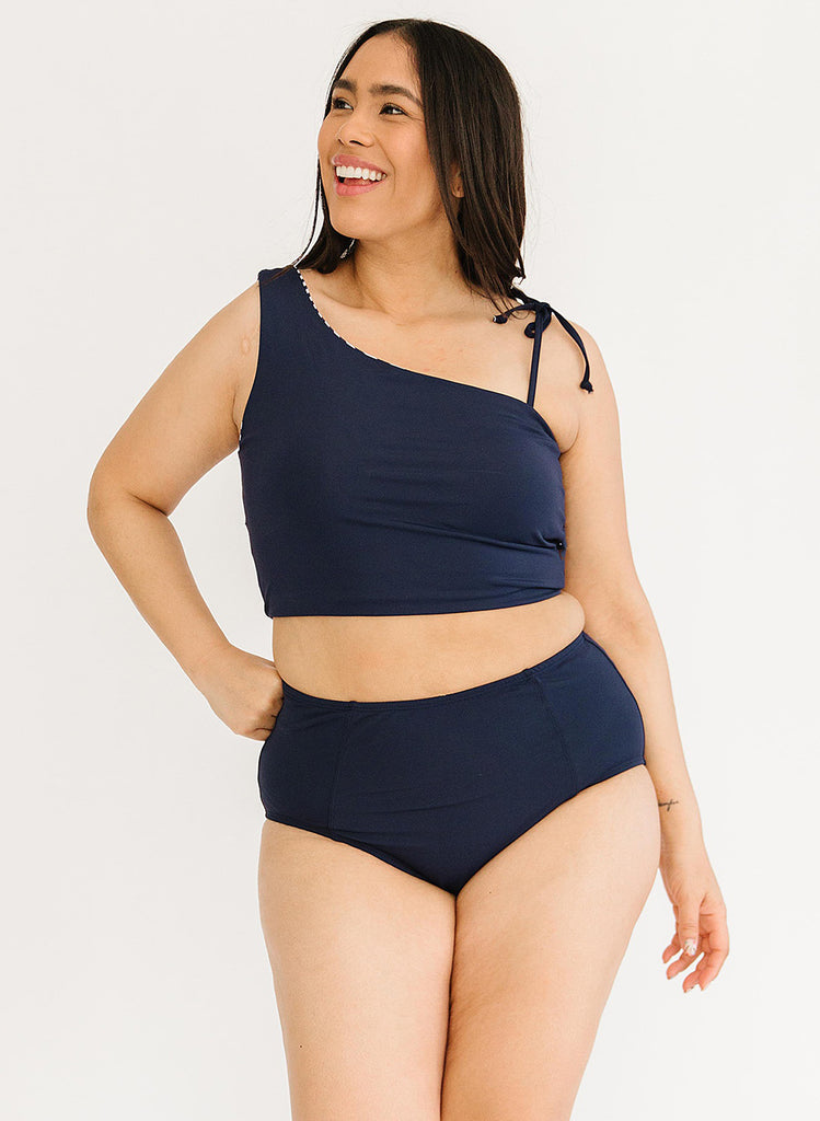 Photo of a woman with her hand on her hip wearing a blue cropped swim top with blue high waist swim bottoms
