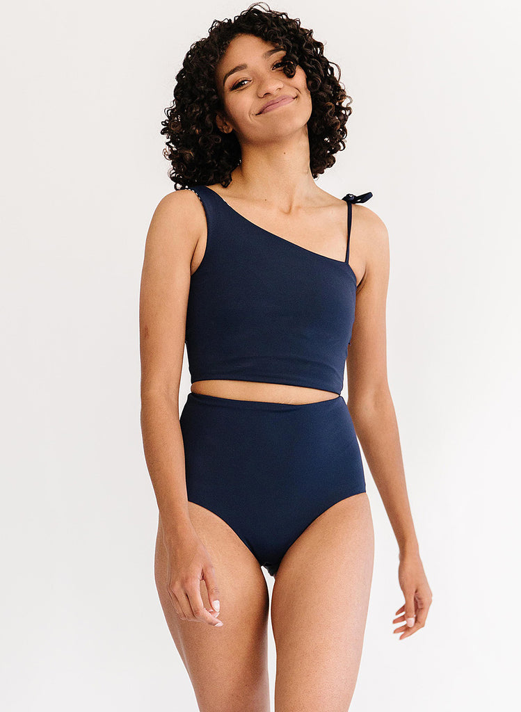 Photo of a woman wearing a midnight blue one-shoulder swim crop top and a midnight blue swim bottom