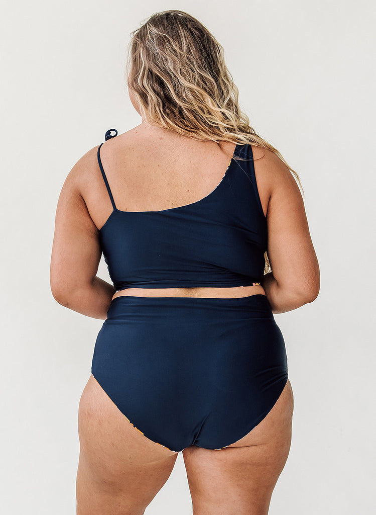 Photo of woman with her back facing us wearing a blue cropped swim top with blue high waist swim bottoms