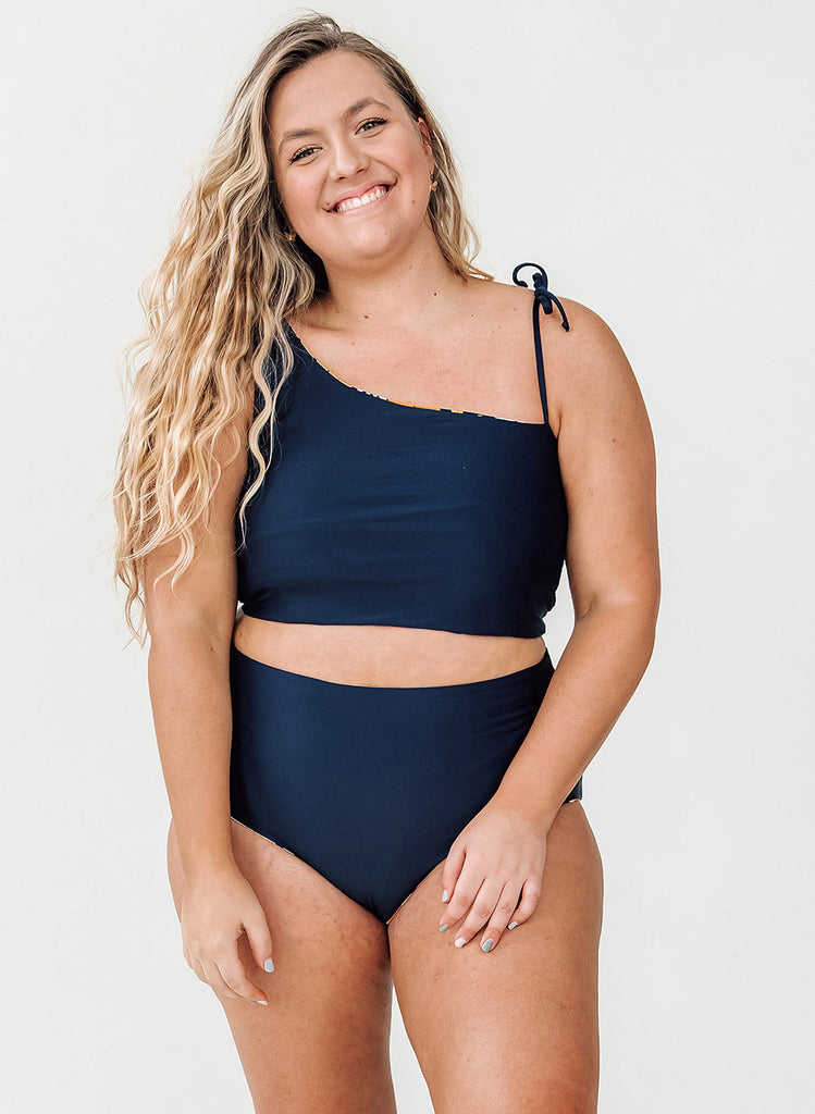 Photo of a woman wearing a midnight blue one-shoulder swim crop top and a midnight blue swim bottom