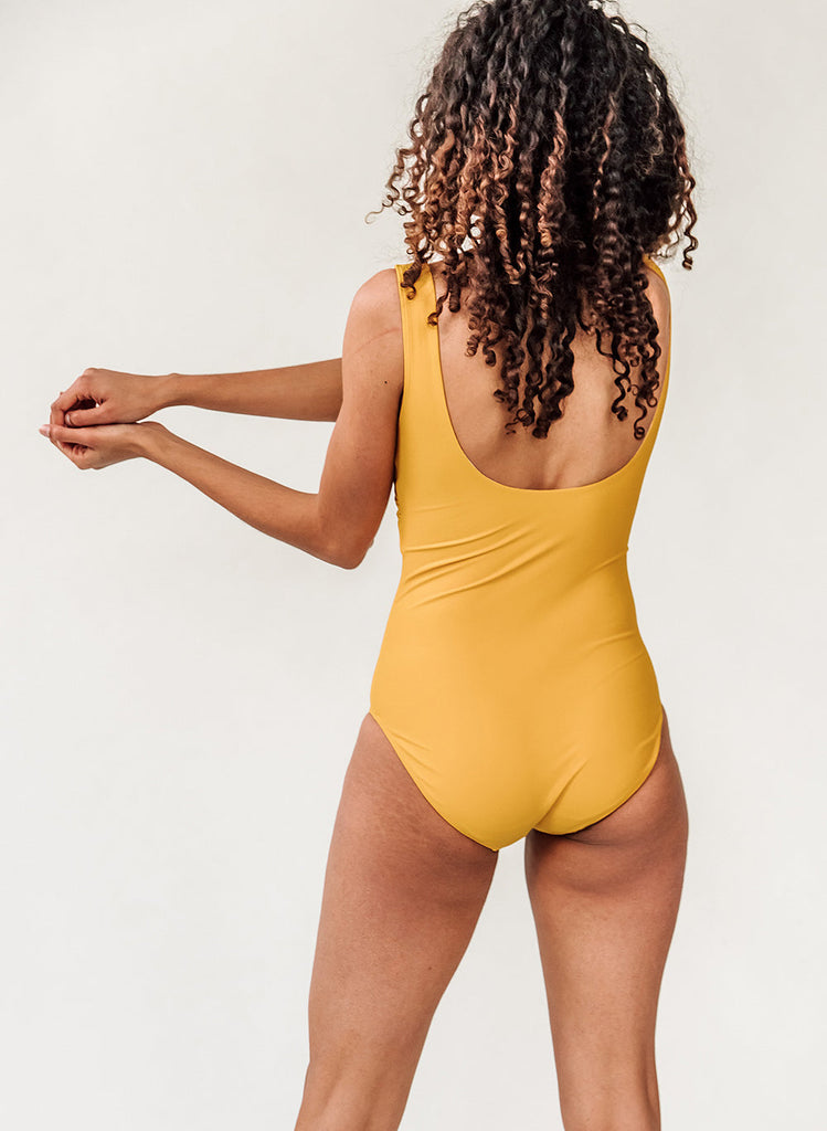 Photo of a woman with her back facing us wearing a yellow one piece swim suit