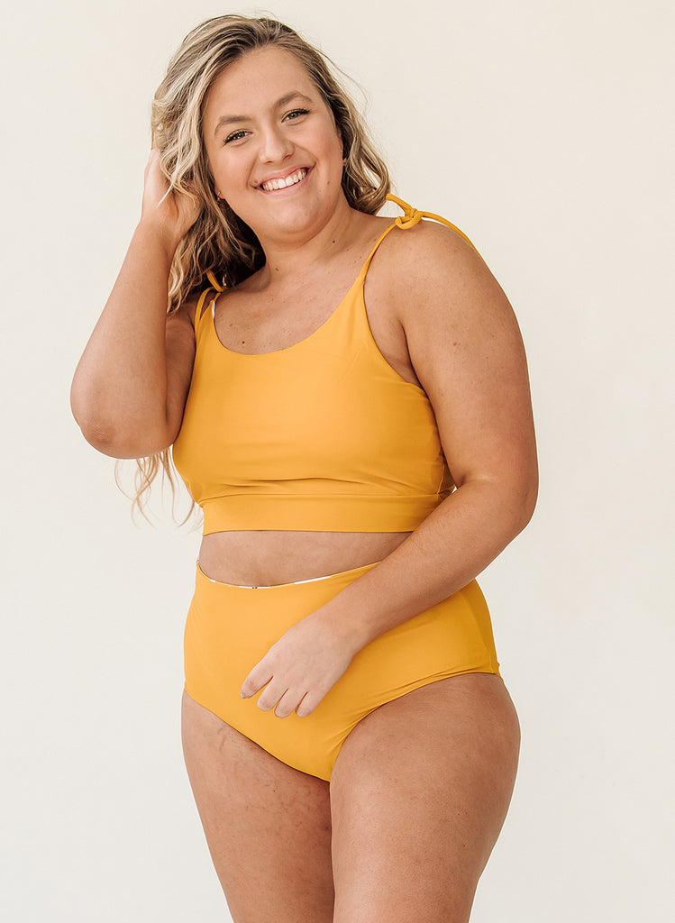 Photo of woman wearing yellow cropped swim top with yellow high waist swim bottoms