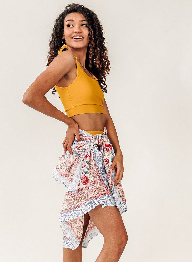 Photo of a woman with her hand on her hip wearing a yellow cropped swim top with a multi colored sarong