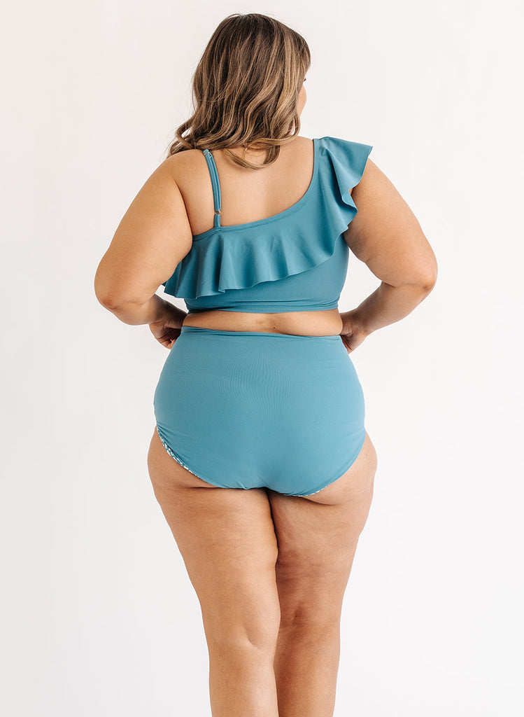 Photo of woman wearing blue ruffle cropped swim top with blue swim bottoms back angle