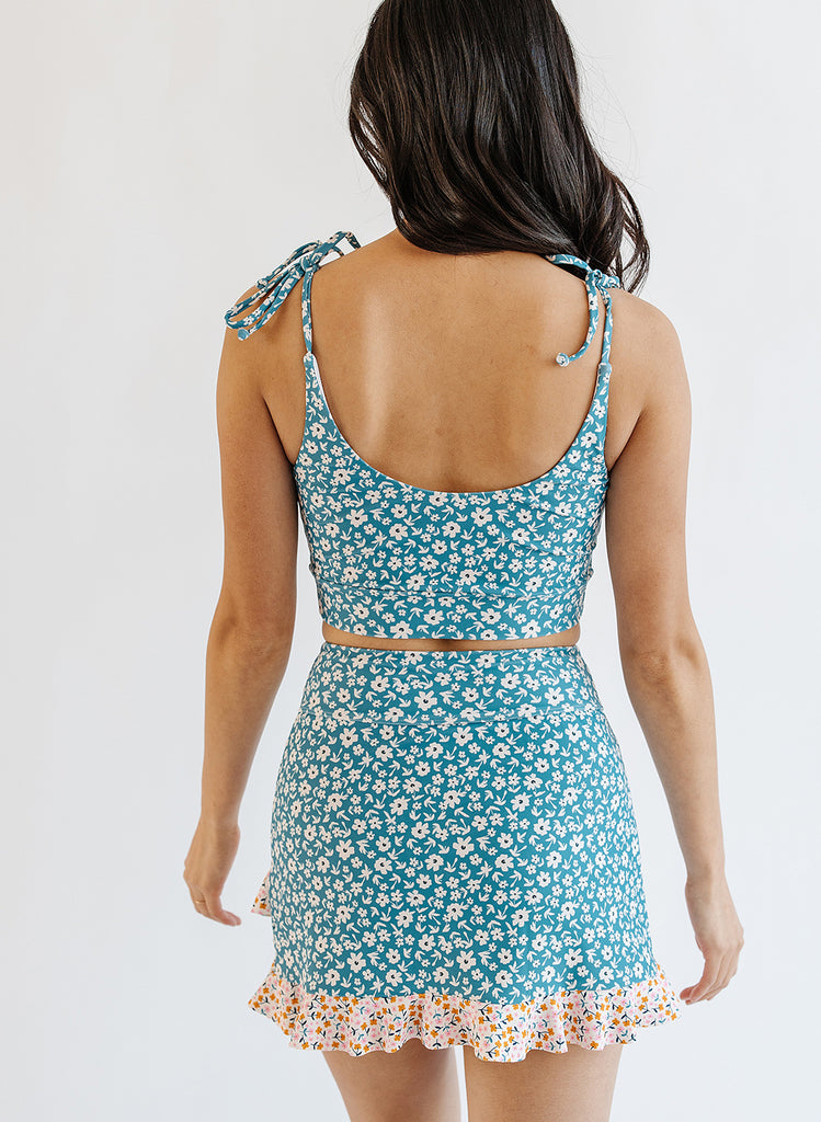 Photo of woman wearing blue floral cropped swim top with blue floral swim skirt back angle