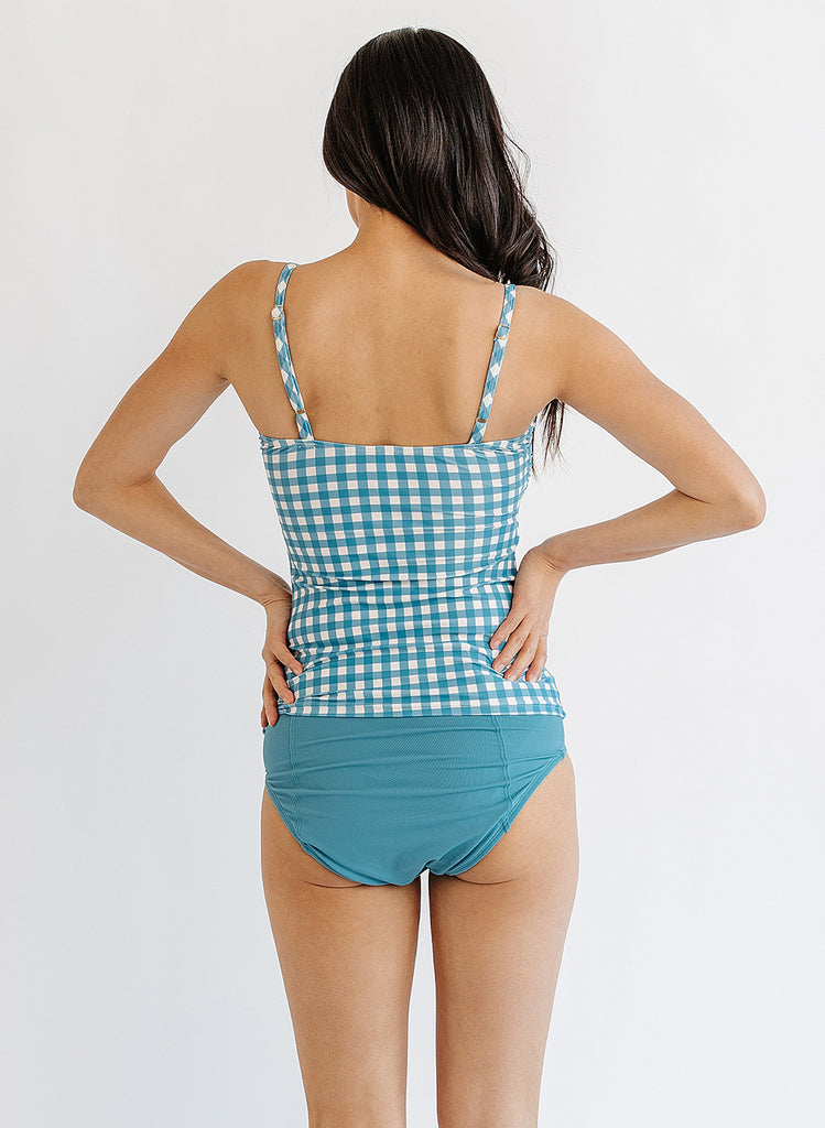 Photo of woman wearing blue and white gingham swim tankini with blue swim bottoms back angle