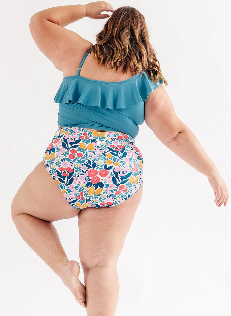 Photo of woman wearing blue ruffle cropped swim top with multi color floral swim bottoms back angle