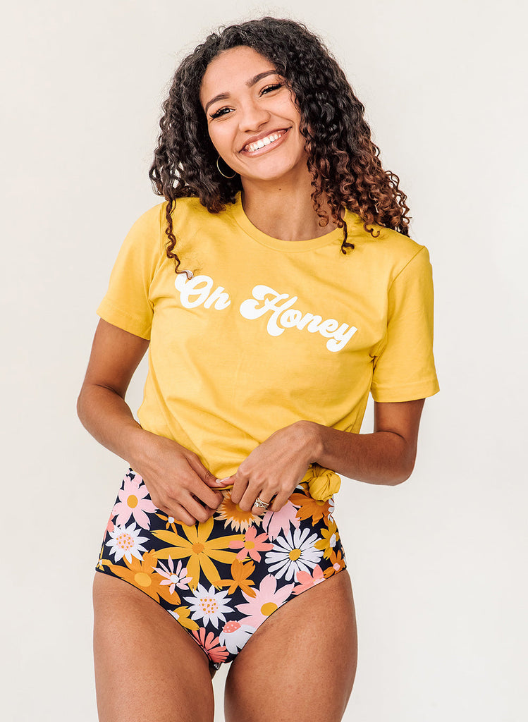 Photo of woman wearing yellow "Oh Honey" t-shirt with multi colored floral high waist swim bottoms