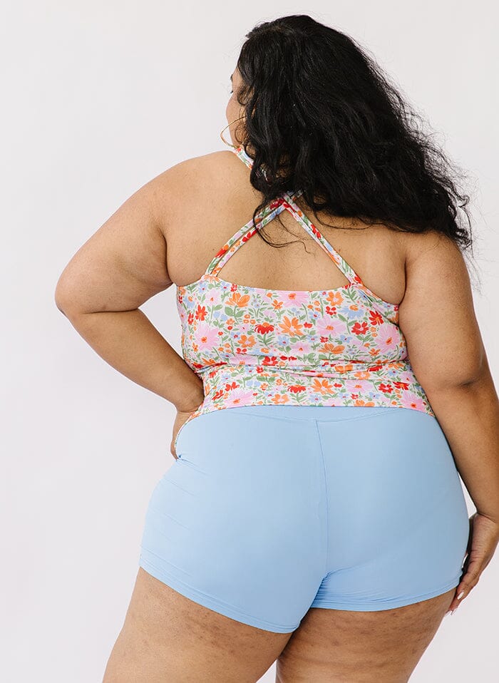 Photo of a woman wearing a floral double cinch swim top and a blue swim short bottom back angle