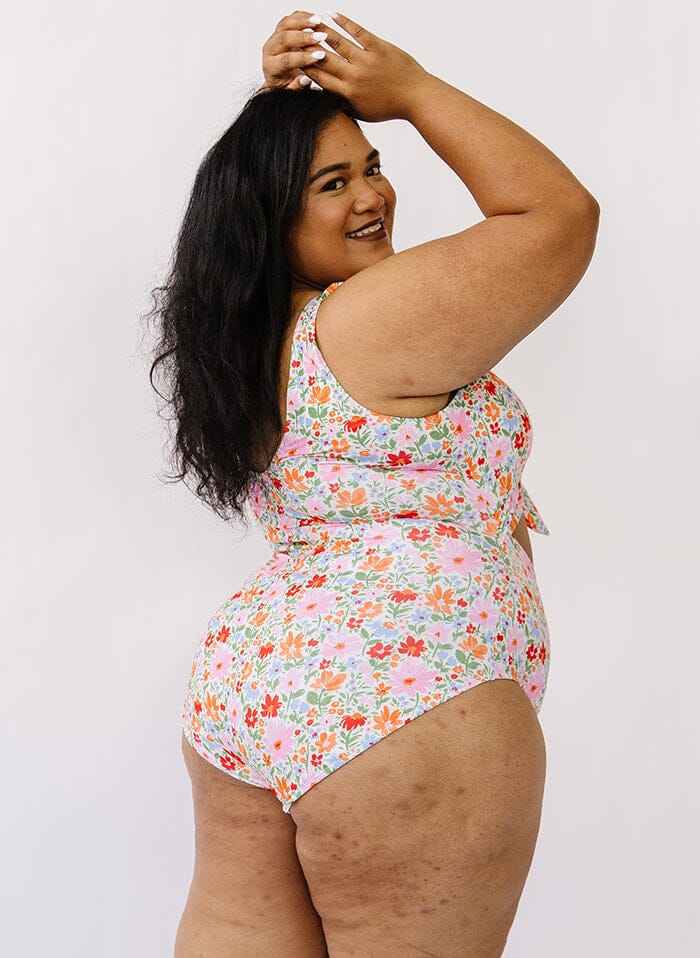 Photo of a woman wearing a floral knotted swim one piece side angle