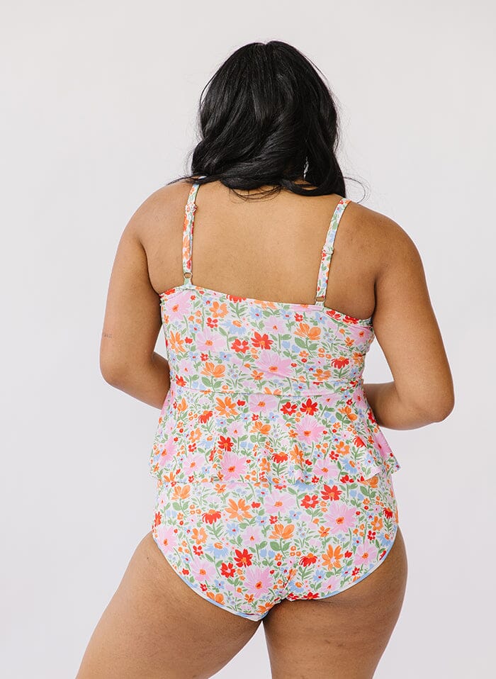 Photo of a woman wearing a floral peplum swim top and a floral swim bottom back angle