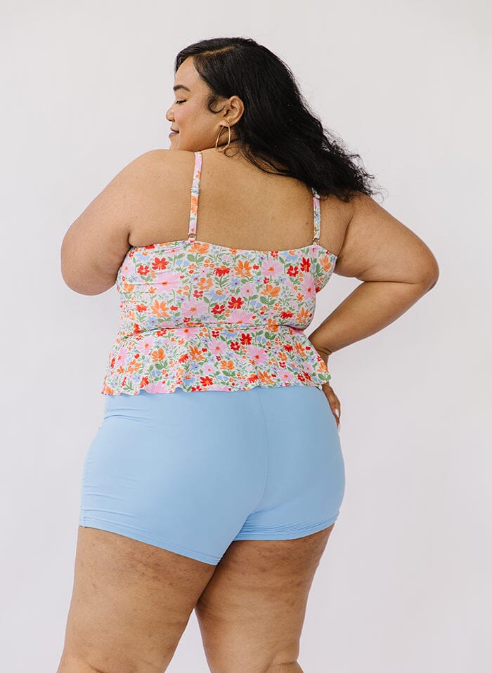 Photo of a woman wearing a floral peplum swim top and a blue swim short bottom back angle