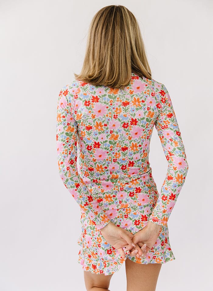 Photo of a woman wearing a floral rash guard swim top and a floral swim skirt bottom back angle
