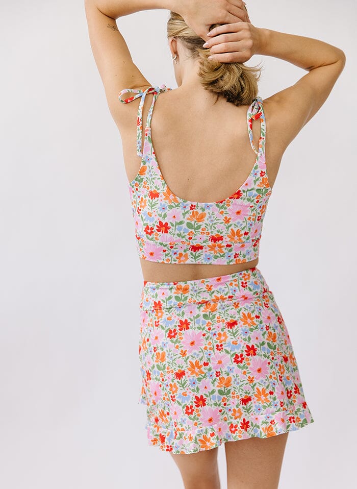 Photo of a woman wearing a floral swim skirt bottom and a floral shoulder-tie swim top back angle