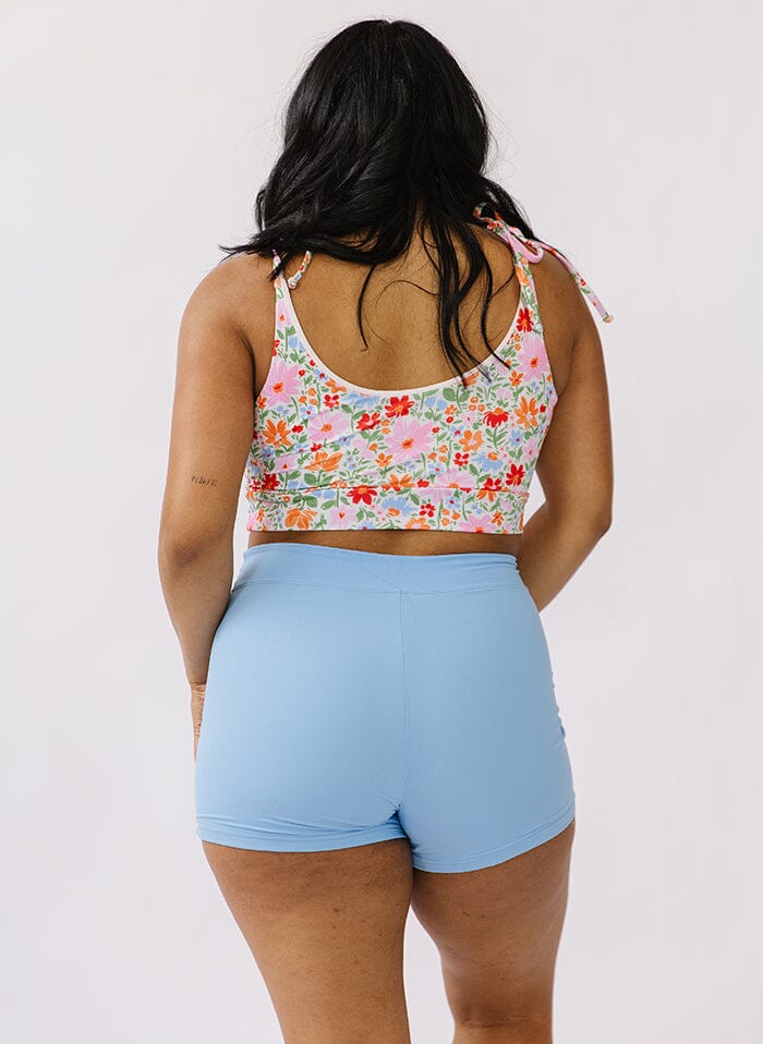 Photo of a woman wearing a floral shoulder-tie swim crop top and a blue swim short bottom back angle